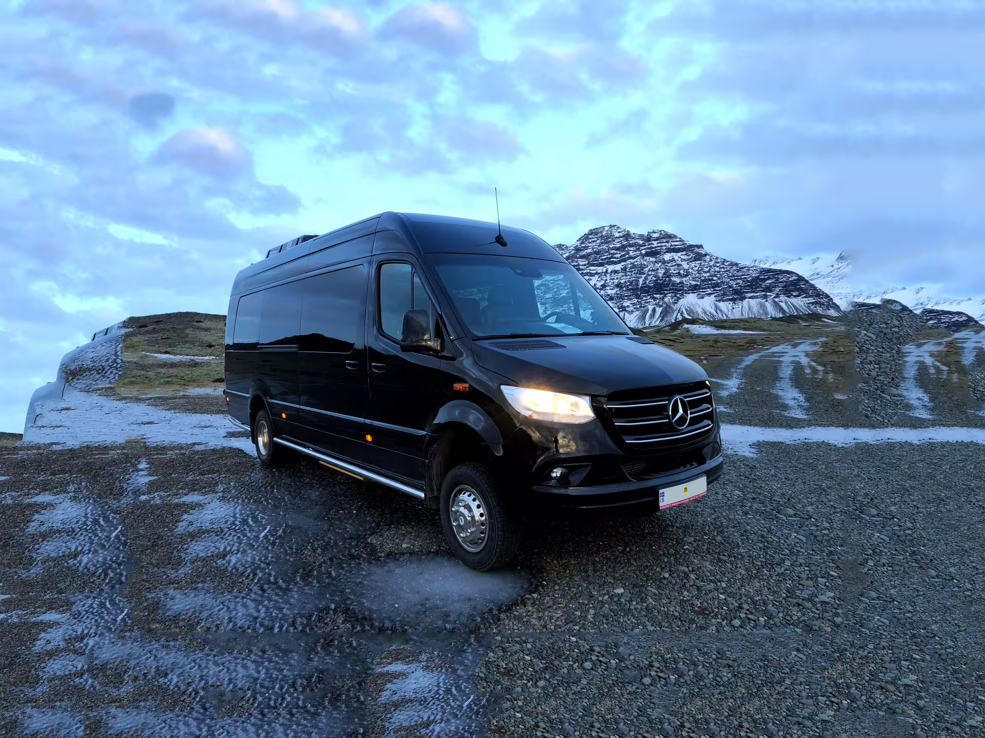 Black Mercedes Sprinter minibus parked on Iceland's snowy south coast with mountain backdrop