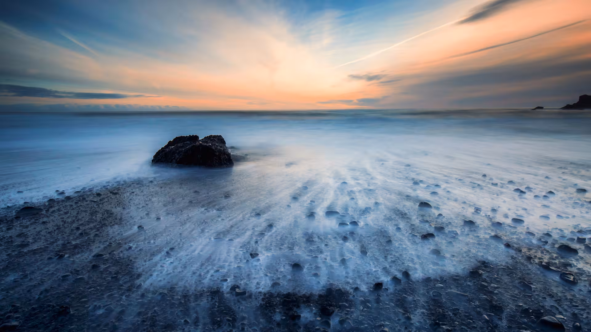 Long exposure of misty waves washing over black pebble beach at sunset on Iceland's South Coast