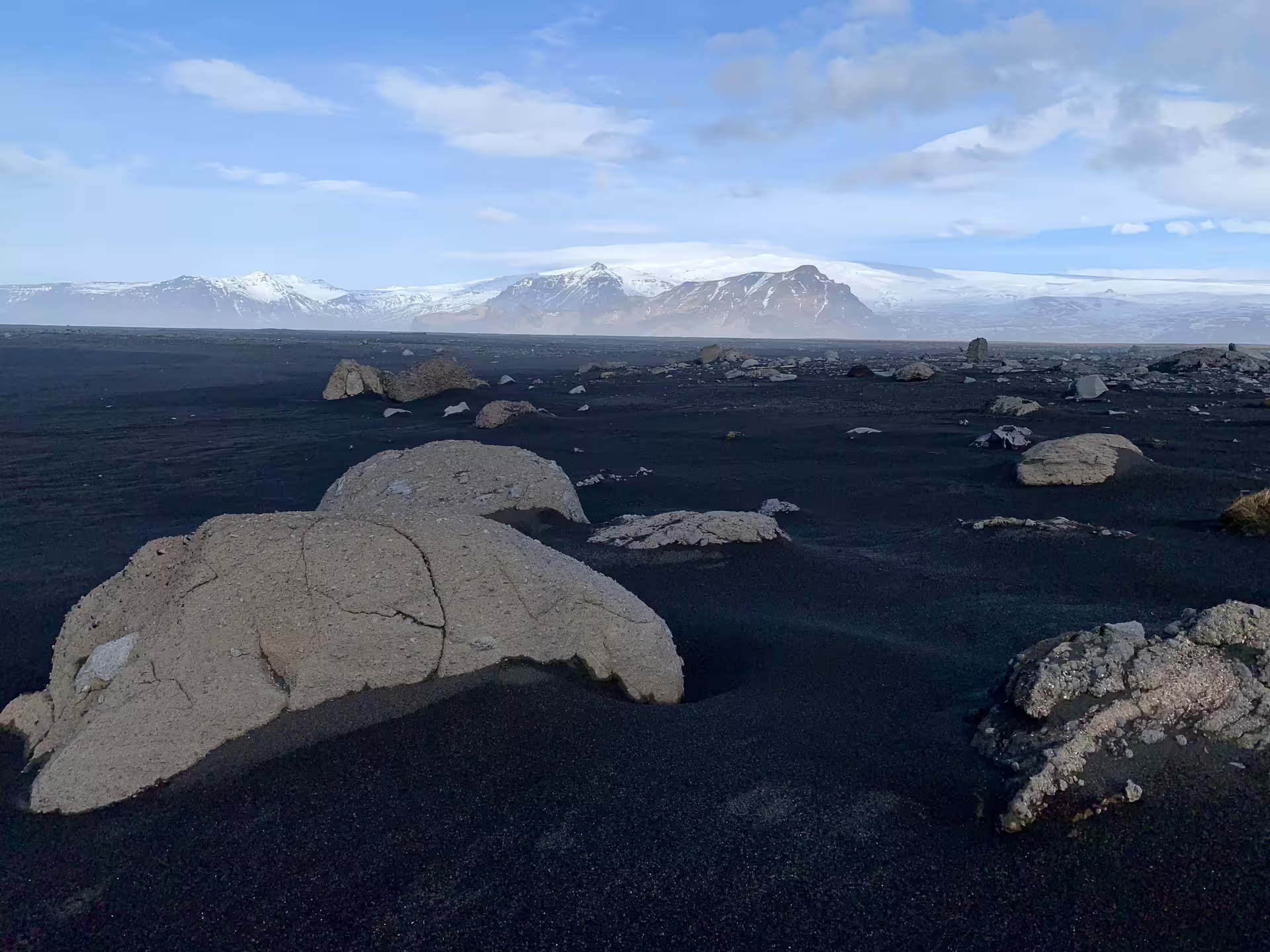 Black sand beach with scattered boulders and snow-capped mountains on Iceland's South Coast