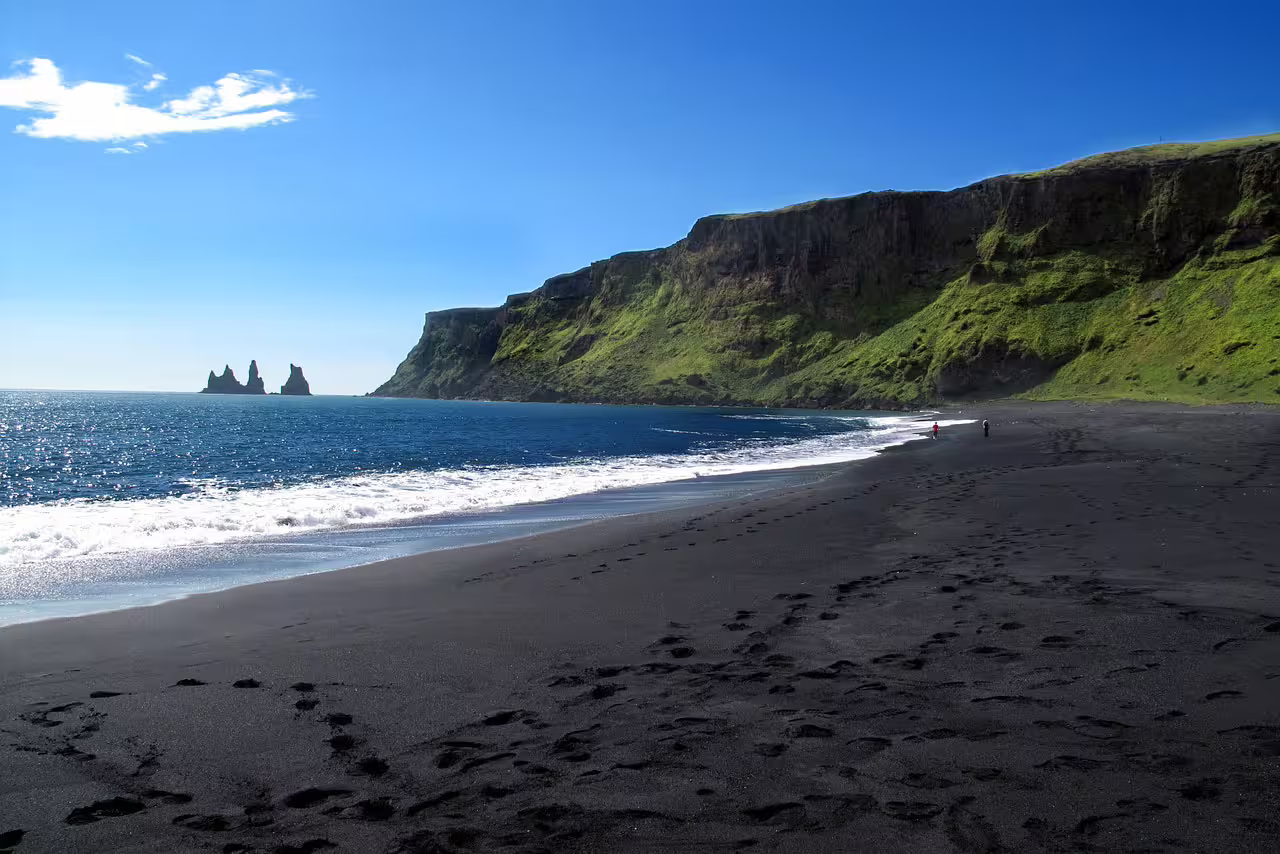 Black sand beach with volcanic rock sea stacks and green cliffs on Iceland's South Coast