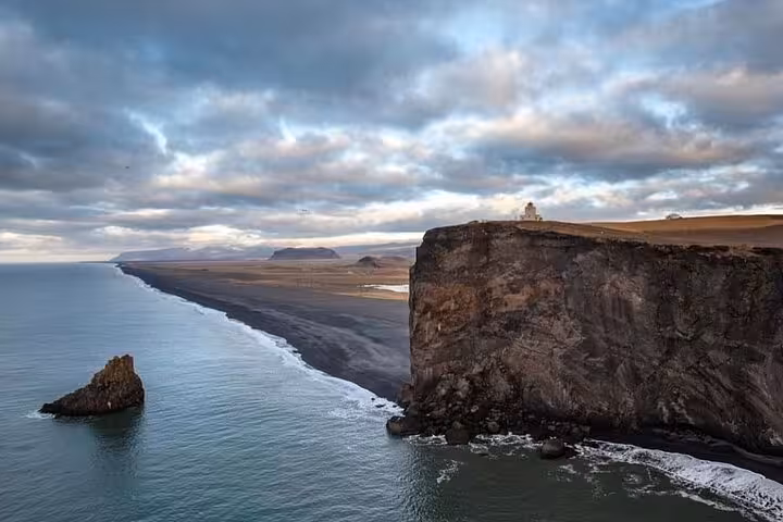Dramatic black sand beach coastline with towering cliffs and lighthouse in Iceland's South Coast