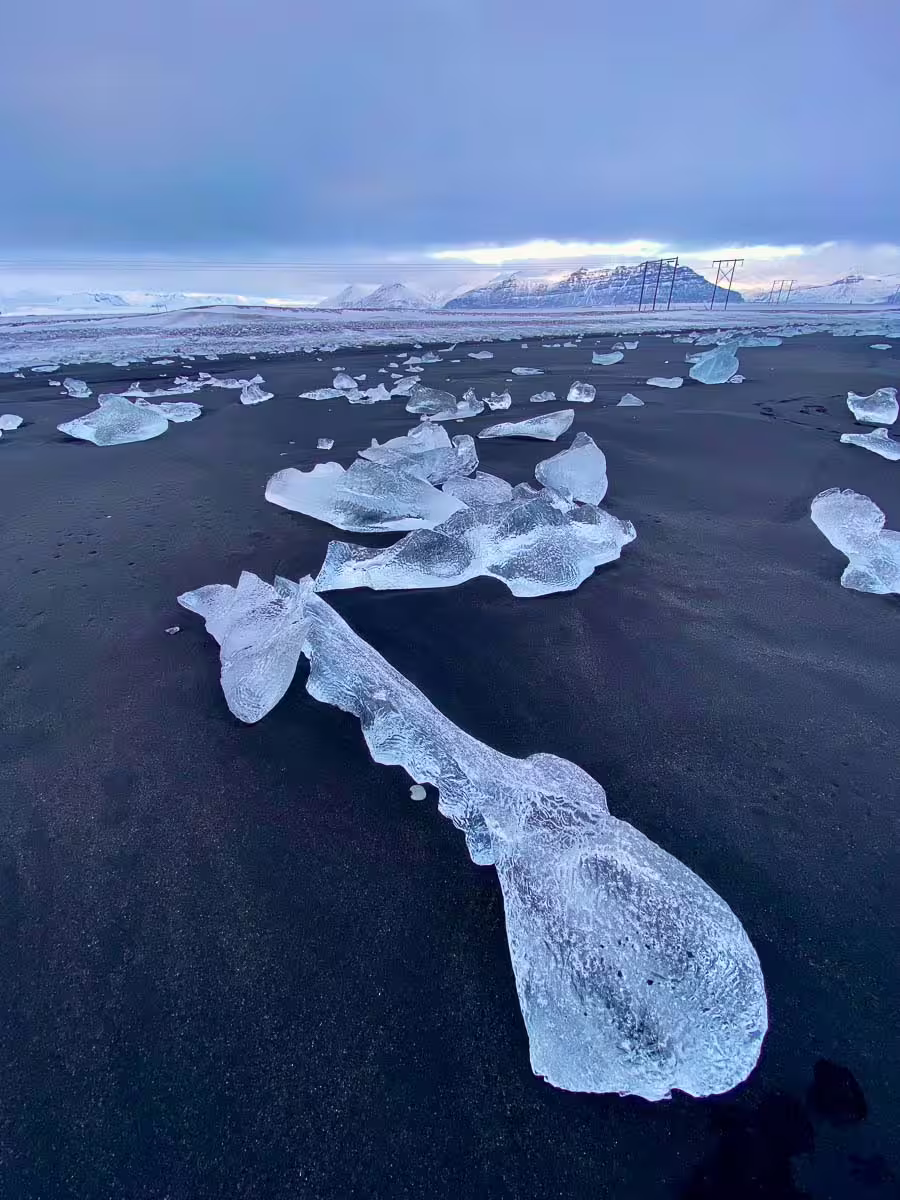 Ice chunks washed ashore on Iceland's black sand beach with snow-capped mountains in background