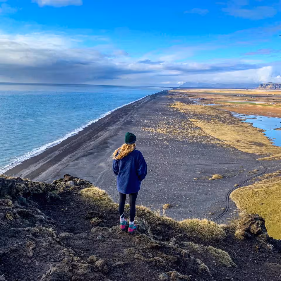 Woman overlooking Iceland's black sand beach and coastline on a sunny day during south coast tour