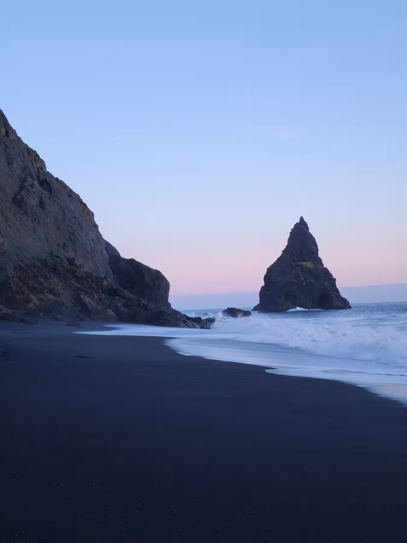 Black sand beach with dramatic sea stack and pink twilight sky on Iceland's south coast
