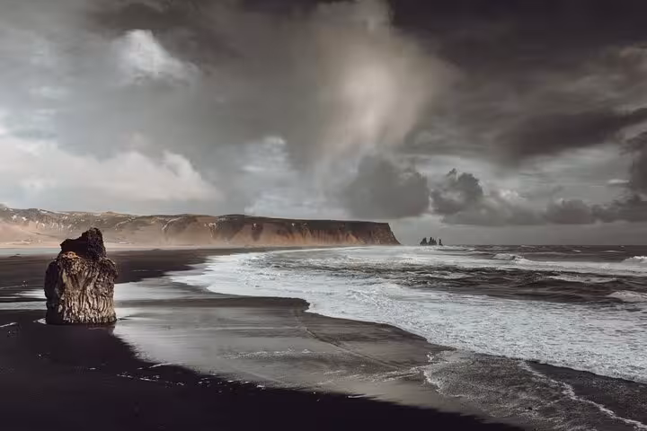 Black sand beach with sea stack rock formation and dramatic stormy skies on Iceland's South Coast