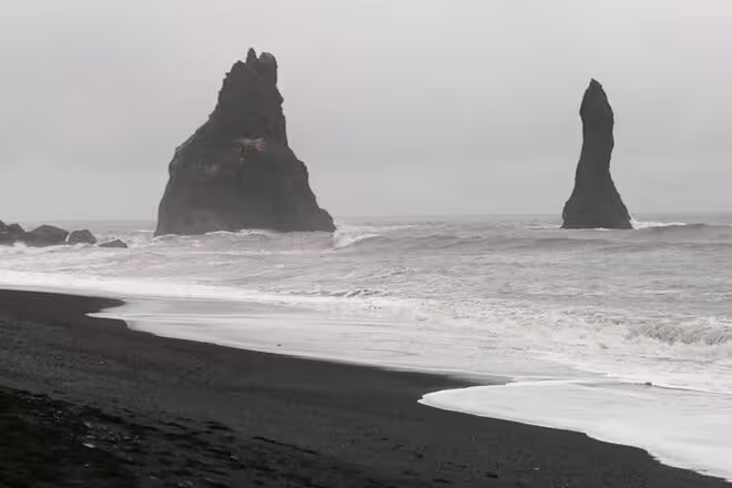 Black sand beach with dramatic basalt sea stacks rising from ocean waves on Iceland's south coast