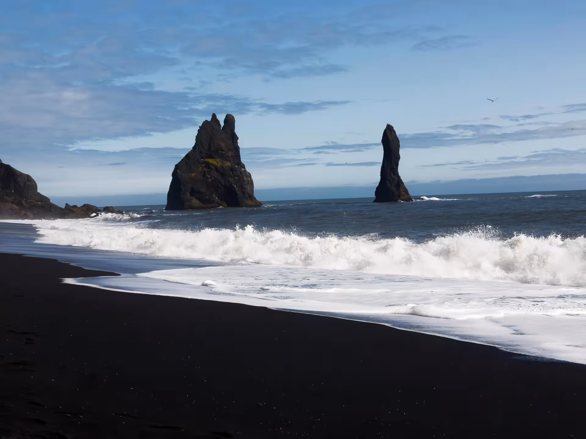 Black sand beach with dramatic sea stacks rising from crashing waves on Iceland's South Coast