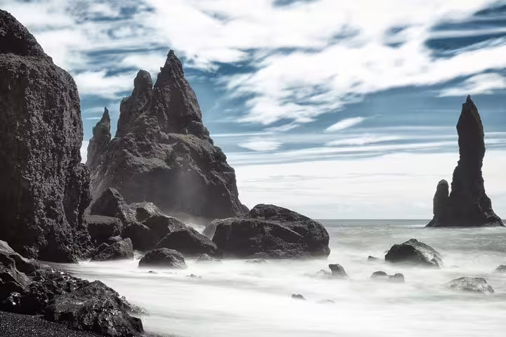 Dramatic black basalt sea stacks rising from misty waves on Iceland's South Coast black sand beach