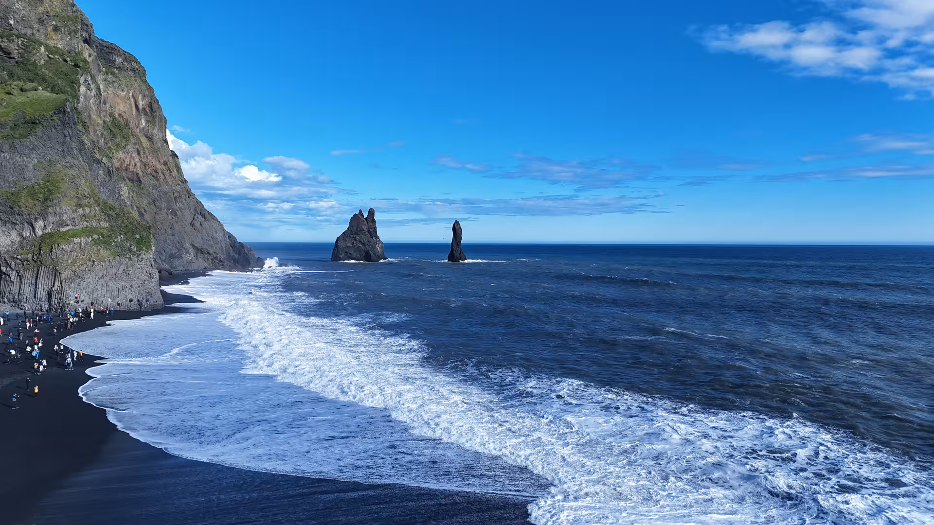 Black sand beach with towering basalt sea stacks and crashing waves along Iceland's south coast