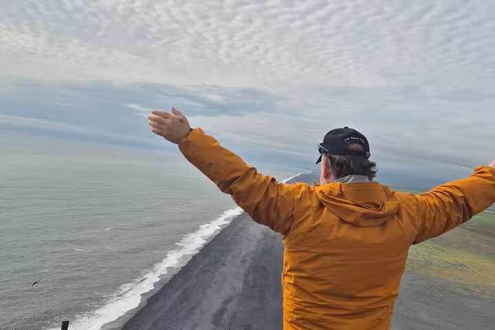 Traveler in orange jacket overlooking Iceland's black sand beach coastline from elevated viewpoint