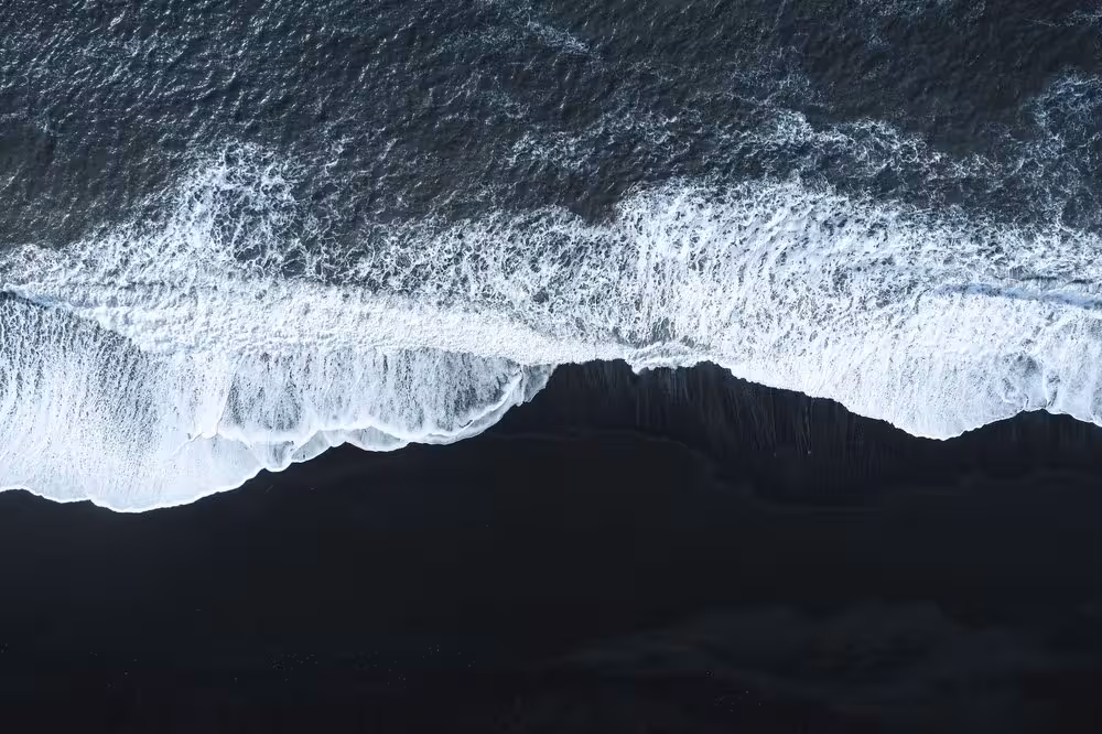 Aerial view of white waves crashing on Iceland's black sand beach along the South Coast