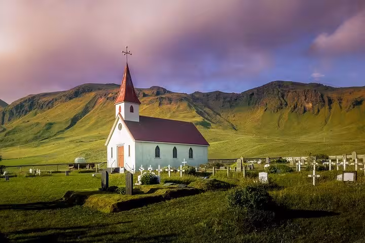 White church with red roof and cemetery surrounded by green hills on Iceland's South Coast
