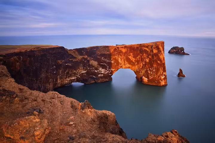 Dramatic red basalt sea arch at Dyrhólaey on Iceland's South Coast with calm teal ocean waters