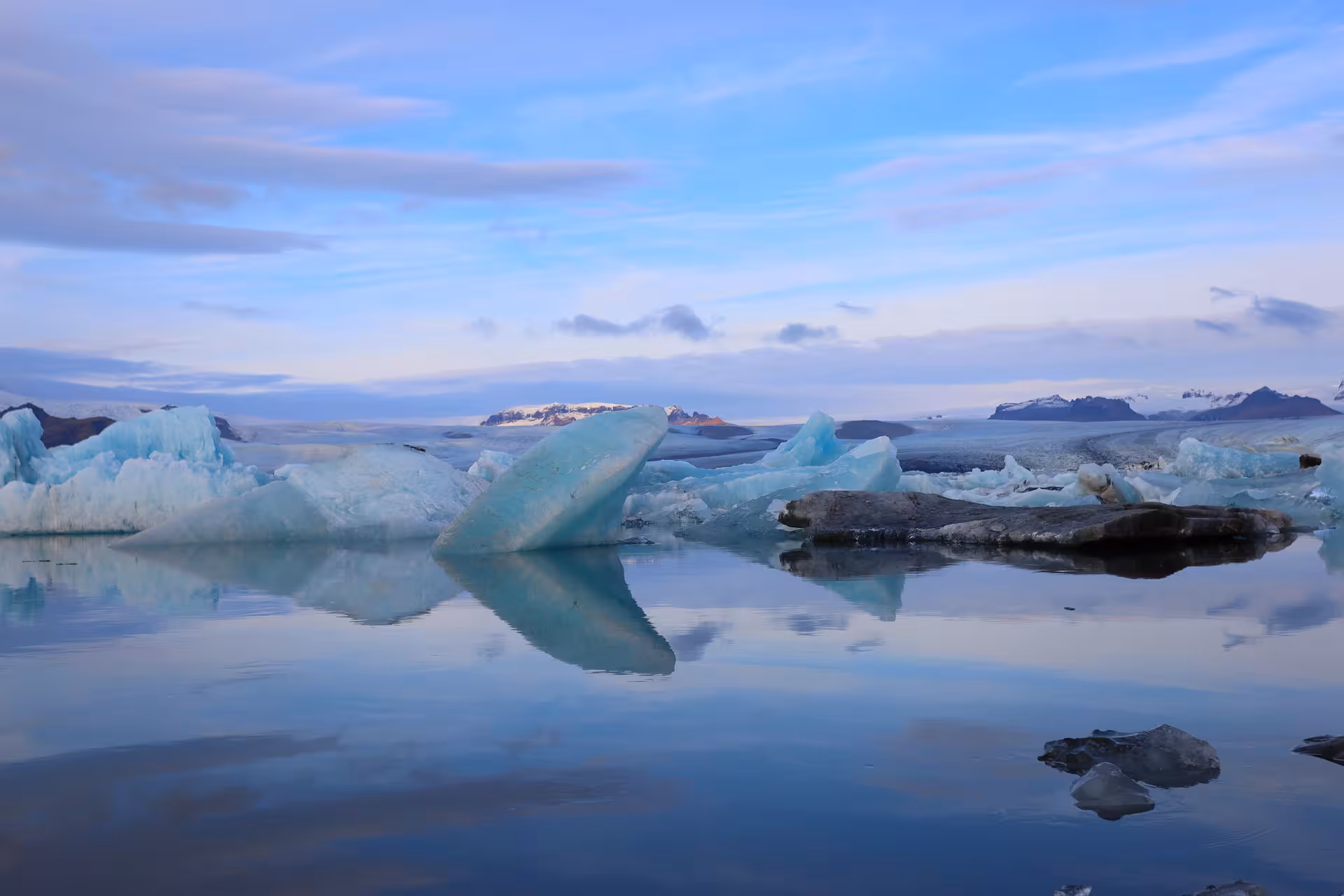 Turquoise icebergs floating on the calm glacial lagoon with snow-capped mountains in Iceland