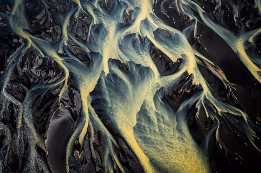 Aerial view of glacial river delta with teal and yellow braided streams over black volcanic sand, Iceland South Coast