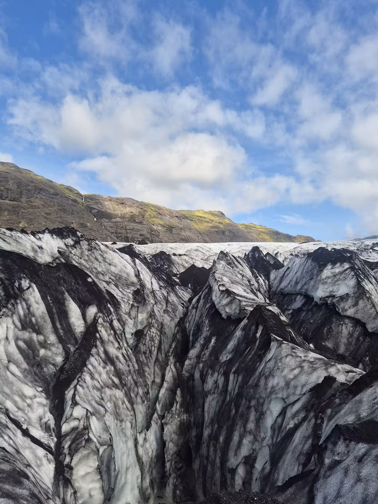 Black ash-streaked glacier ice formations with jagged seracs on Iceland's South Coast under blue sky