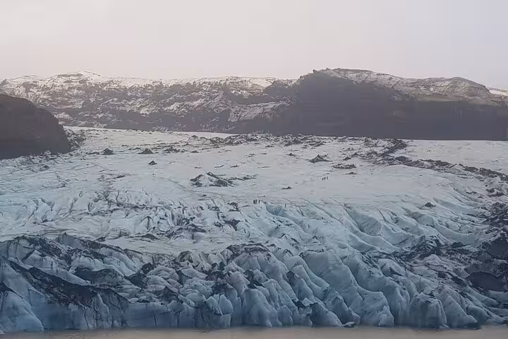 Massive glacier with blue ice formations and dark rocky mountains in Iceland's south coast