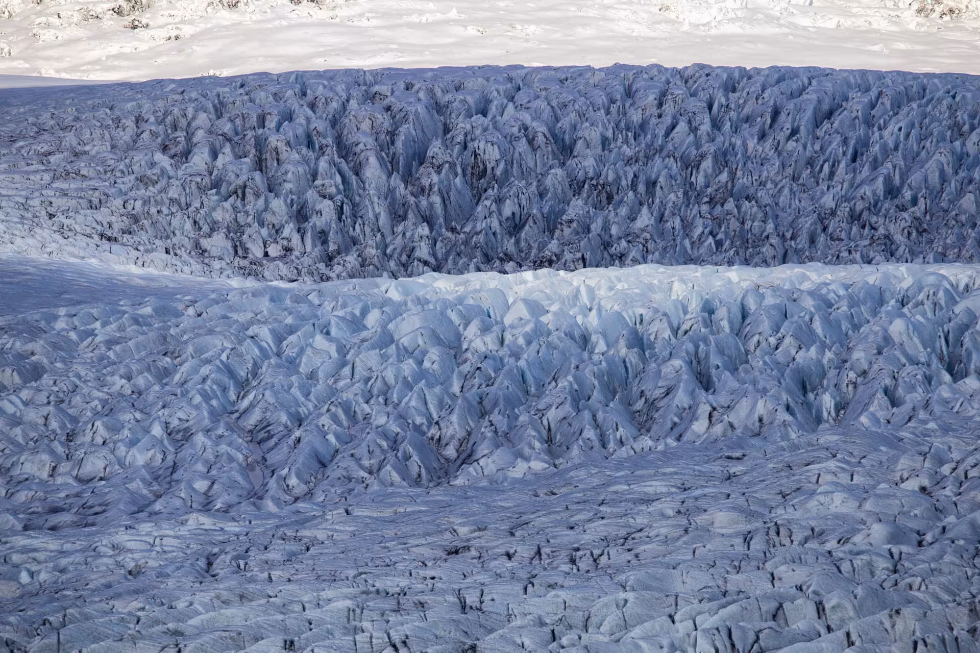 Aerial view of jagged blue ice crevasses on an Icelandic glacier with snow-covered surface above