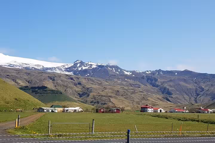 Green farmland with red and white buildings below snow-capped Eyjafjallajökull glacier in South Iceland