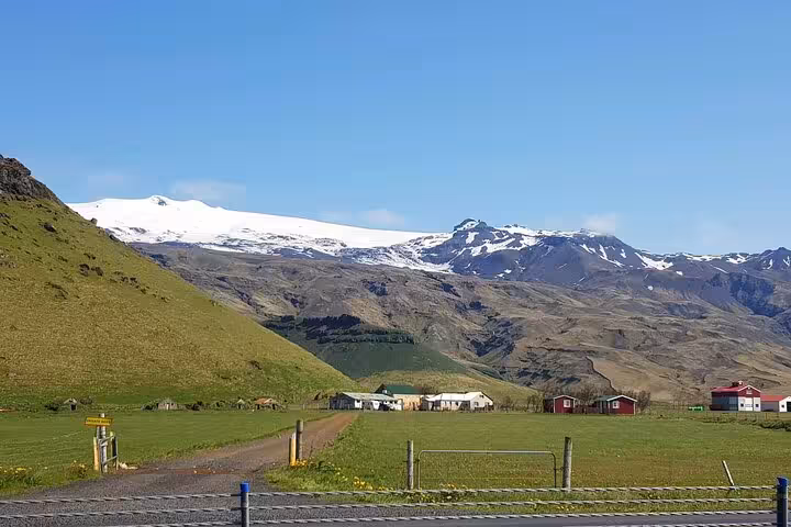 Snow-capped Eyjafjallajökull glacier with green farmland and red barn on Iceland South Coast