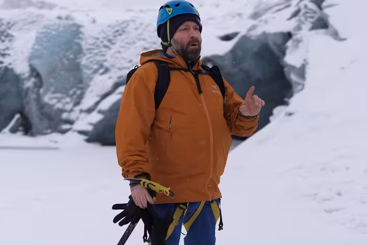 Bearded male glacier guide in orange jacket and blue helmet on Iceland's snowy south coast glacier