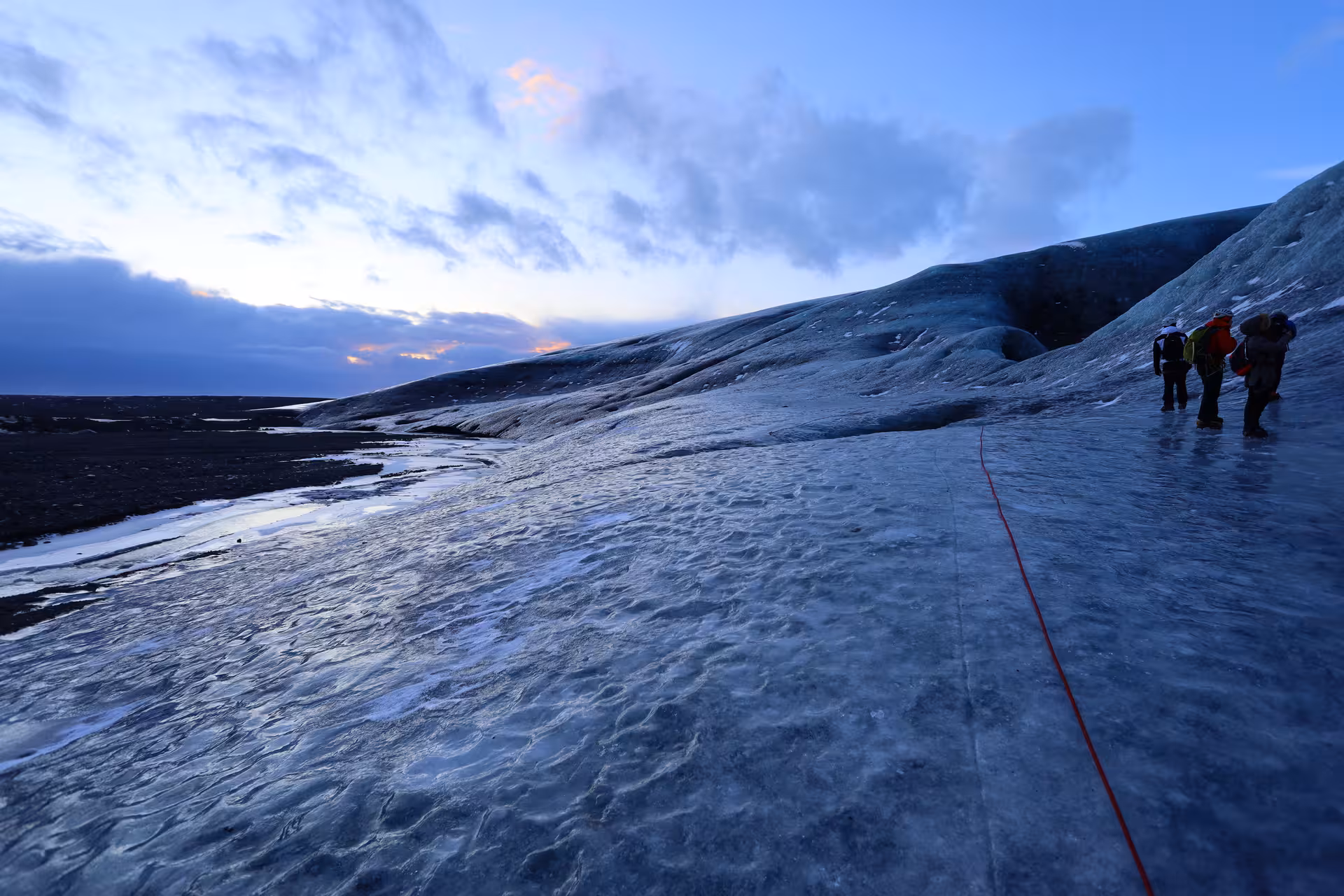 Hikers roped together walking on a glacier in Iceland at dusk with dramatic sky