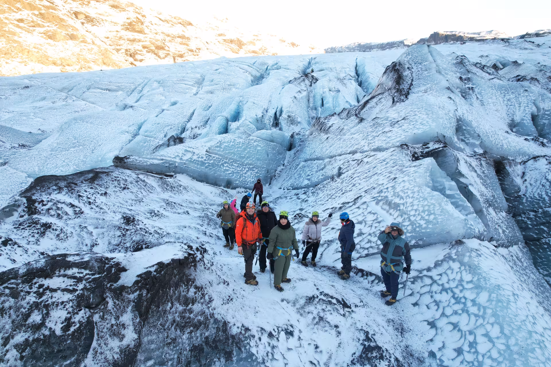 Group of tourists in helmets and harnesses hiking on Iceland glacier with blue ice formations