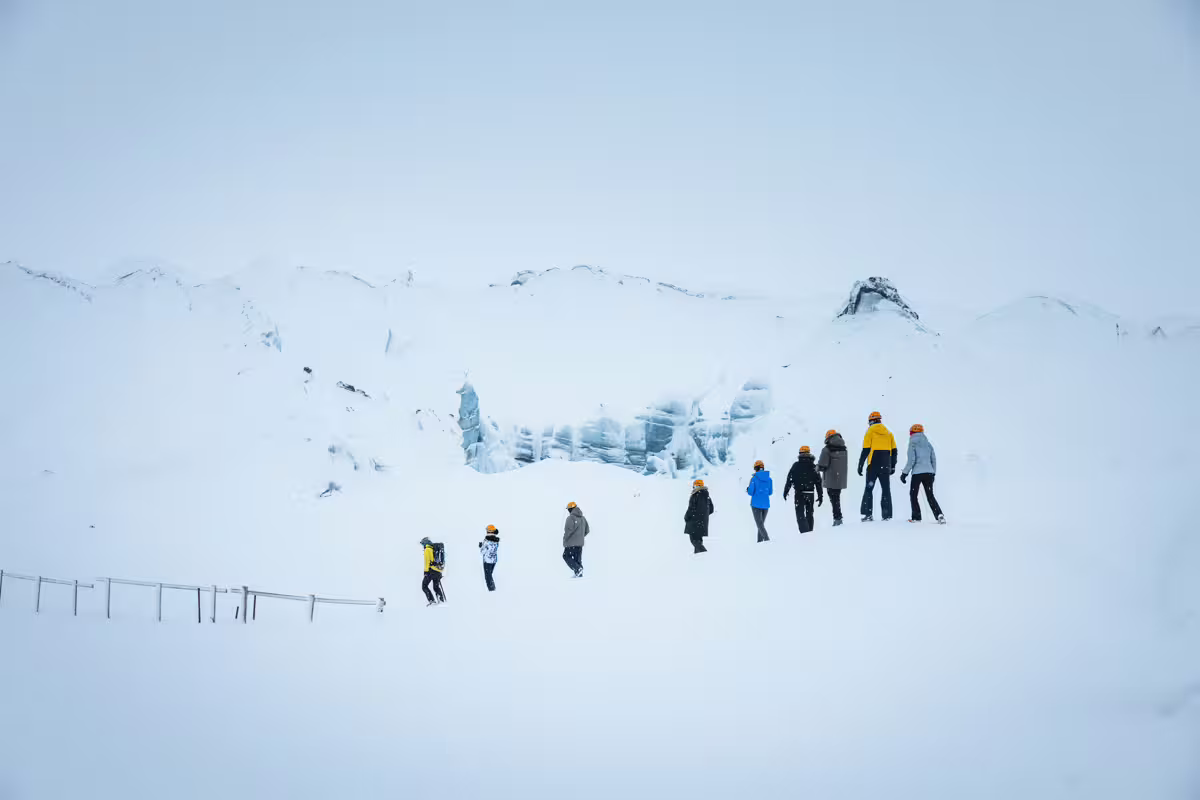 Group of tourists hiking on a snowy glacier toward an ice cave in Iceland