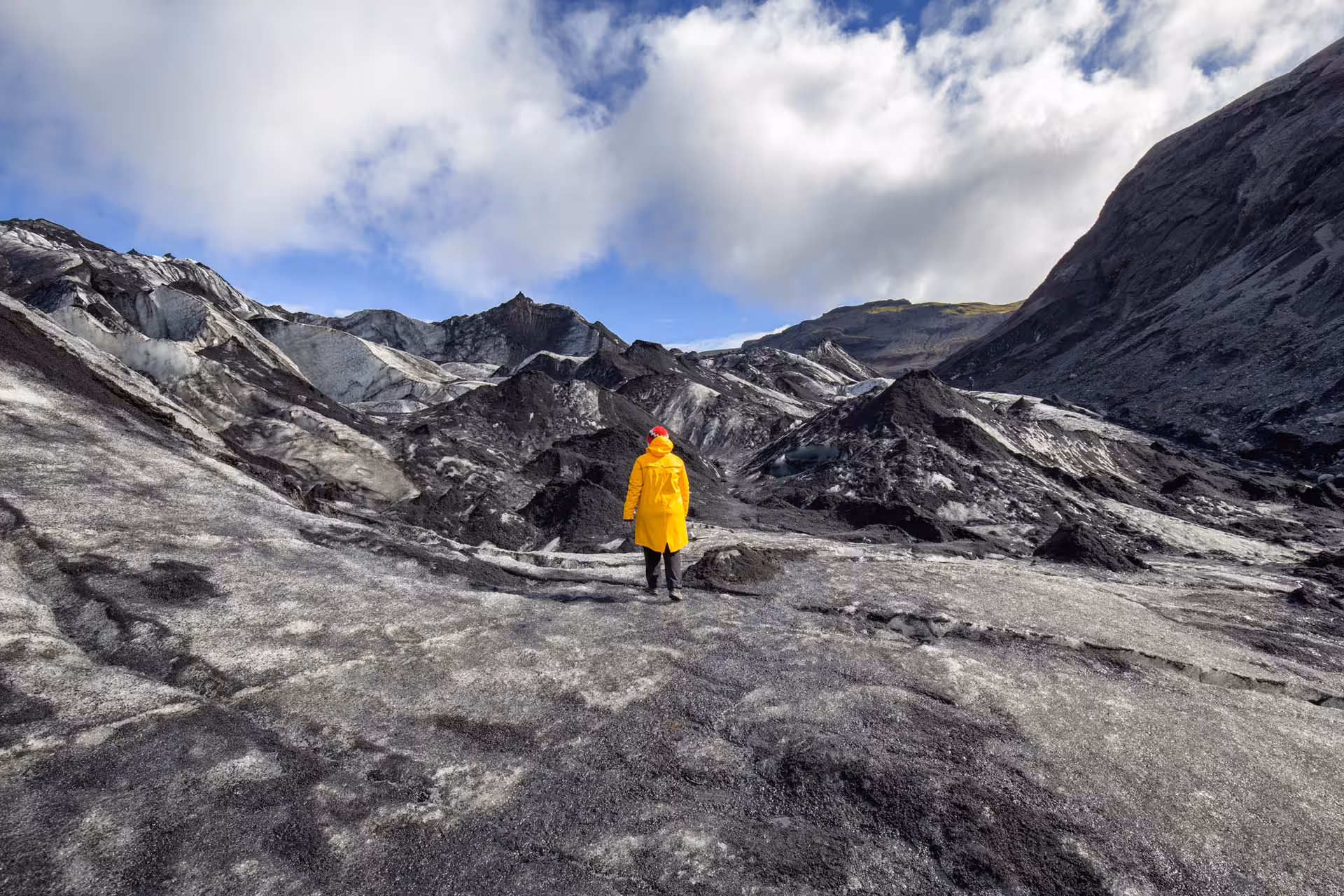 Hiker in yellow jacket standing on black ash-covered glacier on Iceland's South Coast
