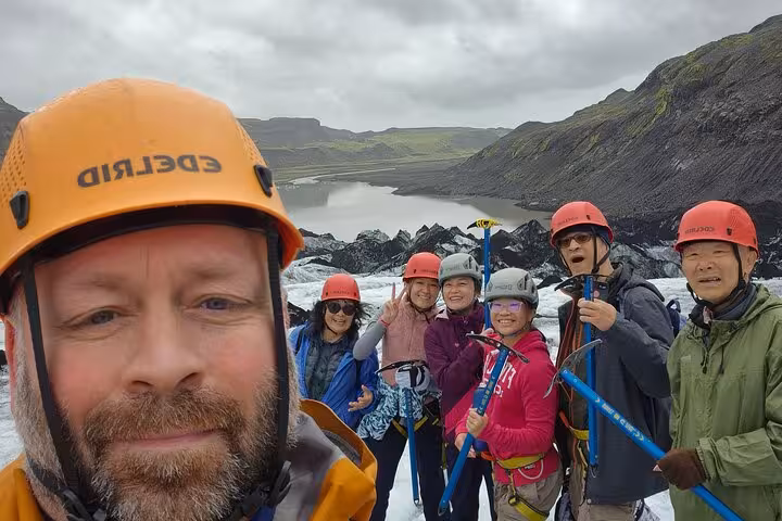 Group of glacier hikers with ice axes and helmets on Iceland glacier with mountain lake backdrop