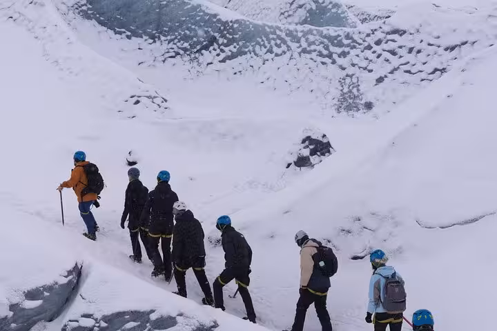 Group of hikers with blue helmets trekking across a snowy glacier in Iceland
