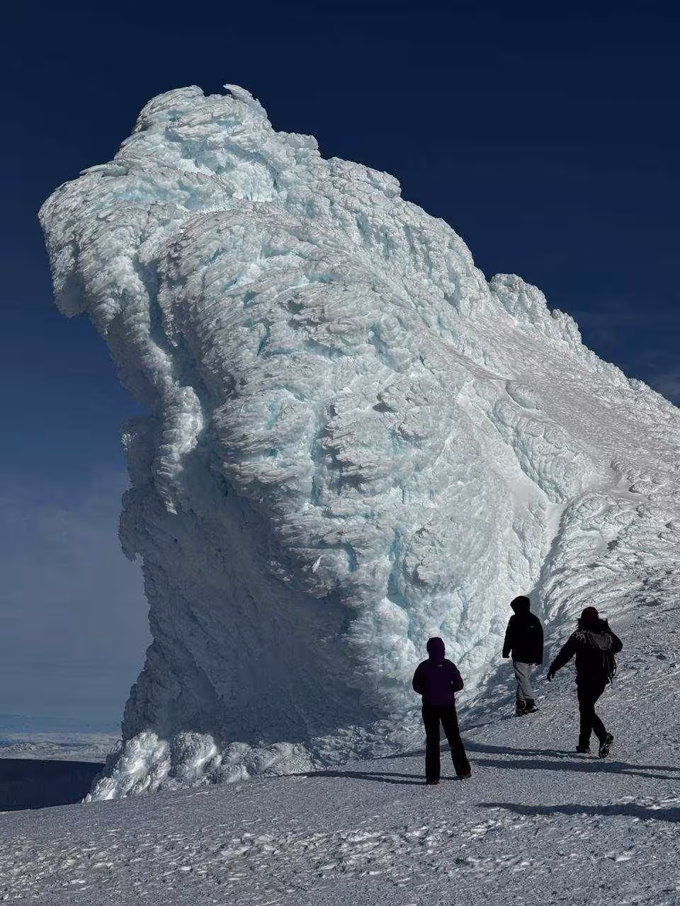 Three tourists standing beside a massive glacial ice formation on Iceland's snowy landscape under clear blue sky