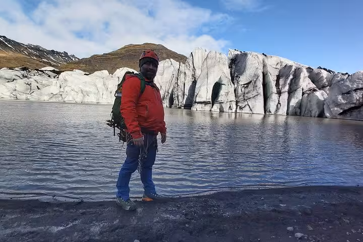 Hiker in red jacket with backpack standing beside glacial lagoon on Iceland South Coast glacier tour