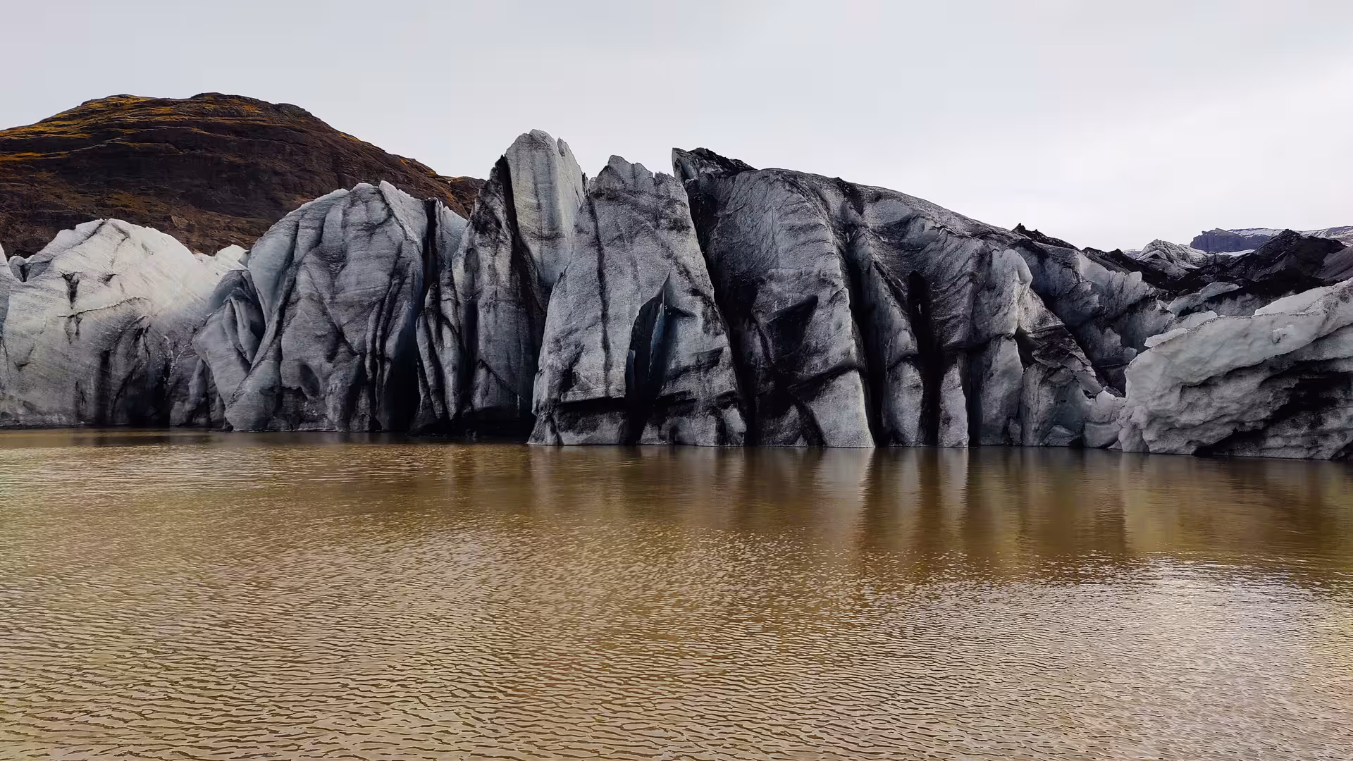 Sediment-streaked glacier ice formations rising from a silty brown glacial lagoon in Iceland