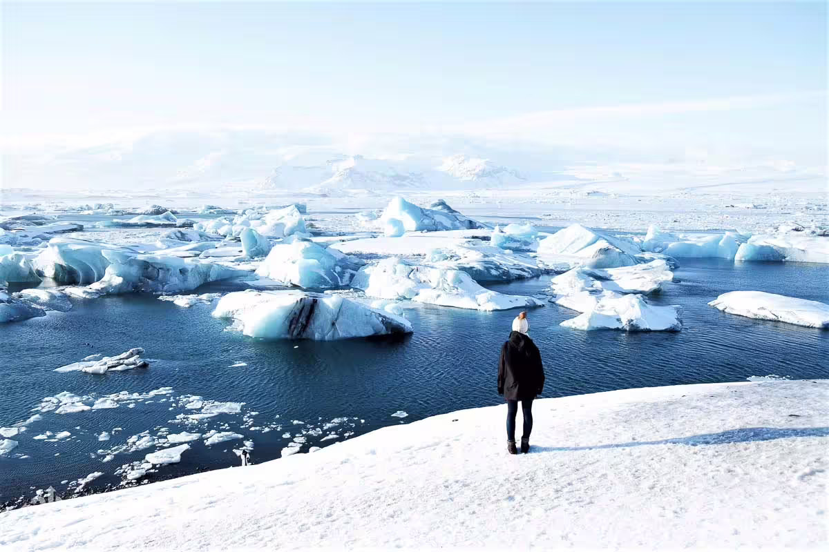 Person standing on snowy shore overlooking Jökulsárlón glacier lagoon with floating icebergs in Iceland