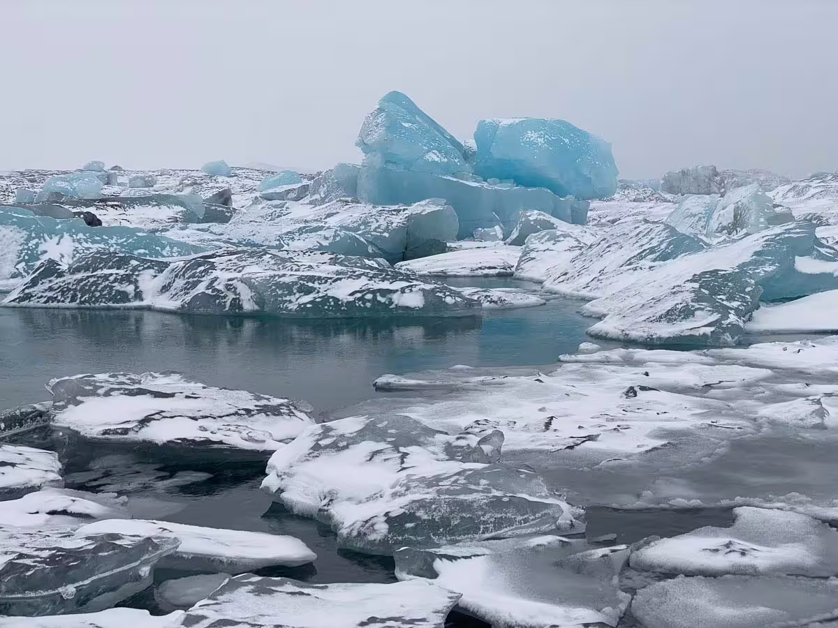 Blue icebergs and snow-covered ice floes floating on a glacial lagoon in Iceland under overcast skies