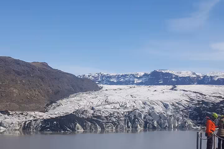Vast glacier flowing into a glacial lagoon with snow-capped mountains and a visitor on a viewing platform in Iceland