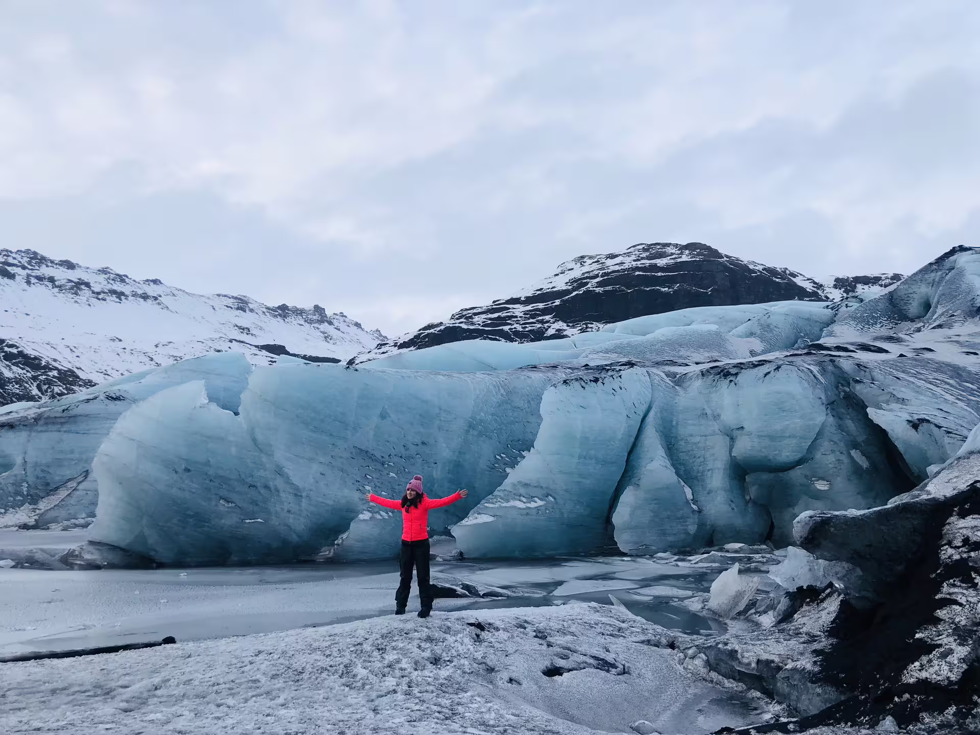 Traveler in red jacket standing before massive blue glacier on Iceland South Coast tour