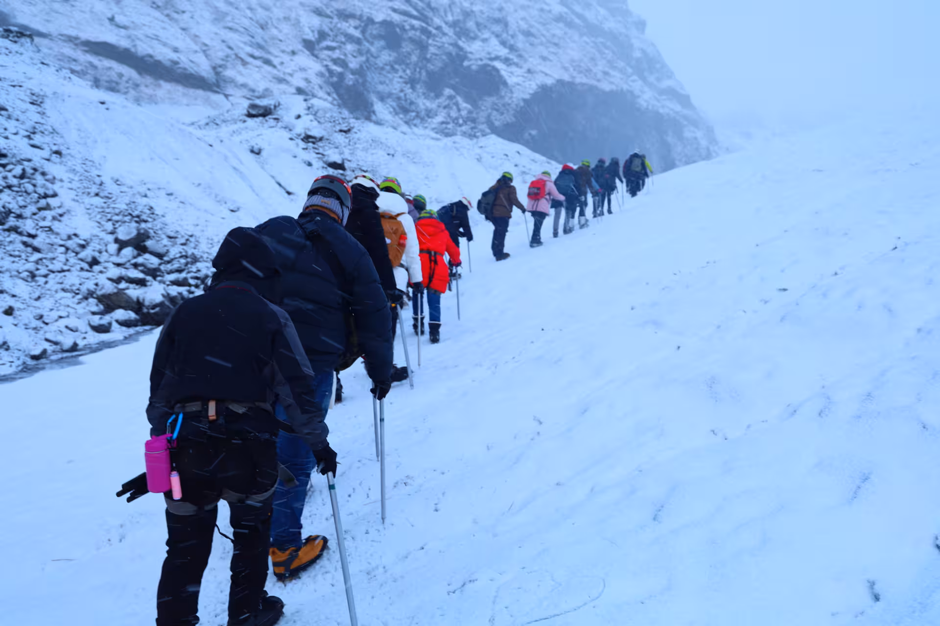 Group of hikers trekking single file through snowy Iceland mountain landscape in winter conditions