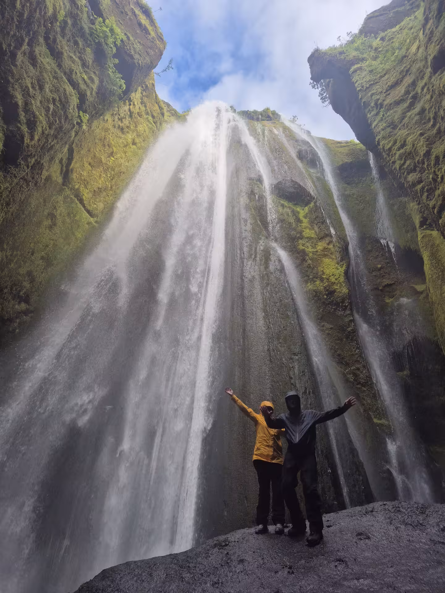 Two tourists with arms raised inside Gljúfrabúi hidden waterfall canyon on Iceland South Coast tour