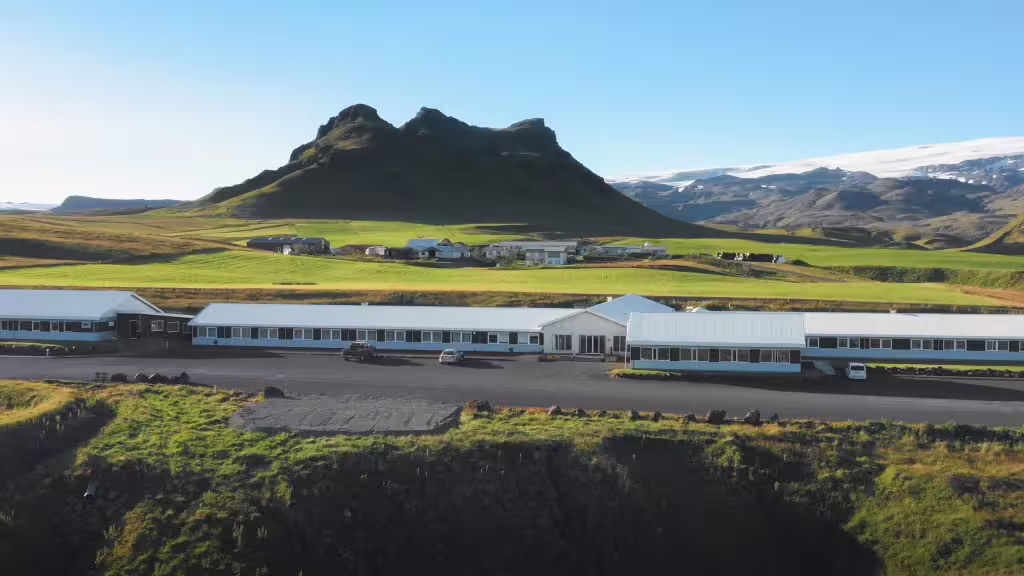 Aerial view of white hotel buildings on Iceland's South Coast with dramatic volcanic mountain and green fields