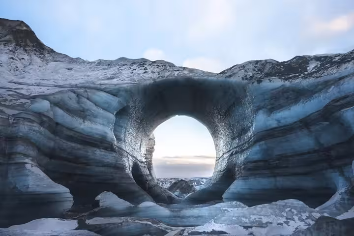 Circular ice cave arch in Iceland with glacial blue walls and sky visible through the opening