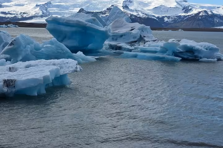 Blue icebergs floating in glacial lagoon with snow-capped mountains in background, Iceland south coast