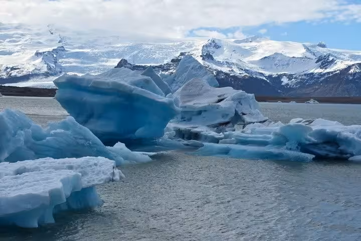 Blue icebergs floating on glacial lagoon with snow-capped mountains in background, Iceland south coast
