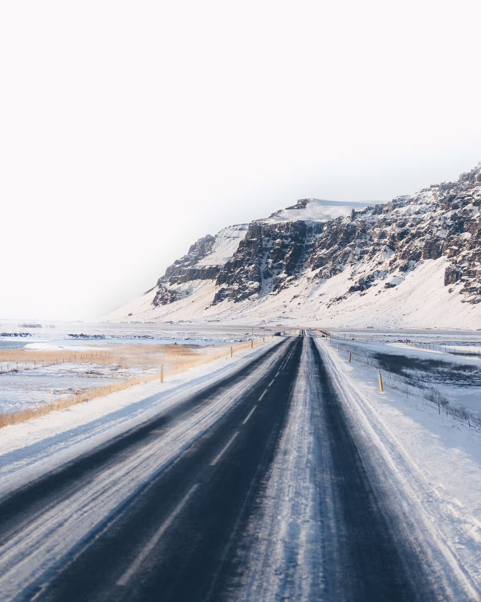 Icy two-lane road leading toward snow-covered cliffs on Iceland's South Coast in winter