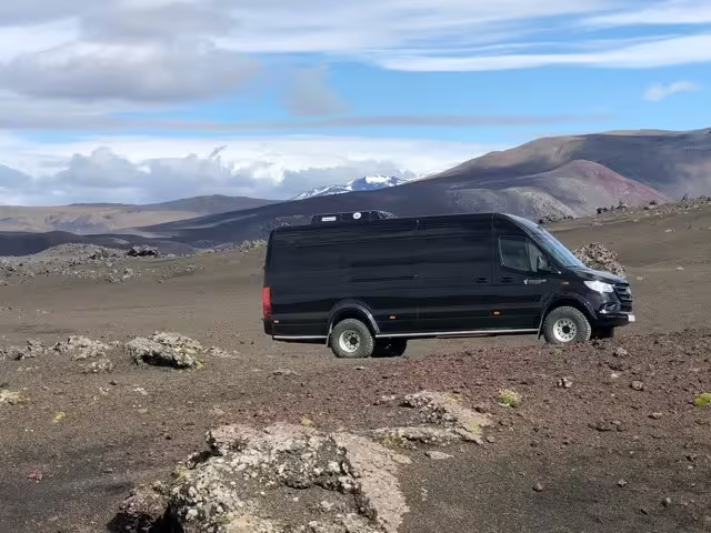 Black 4x4 minibus on volcanic landscape with snow-capped mountains in Iceland