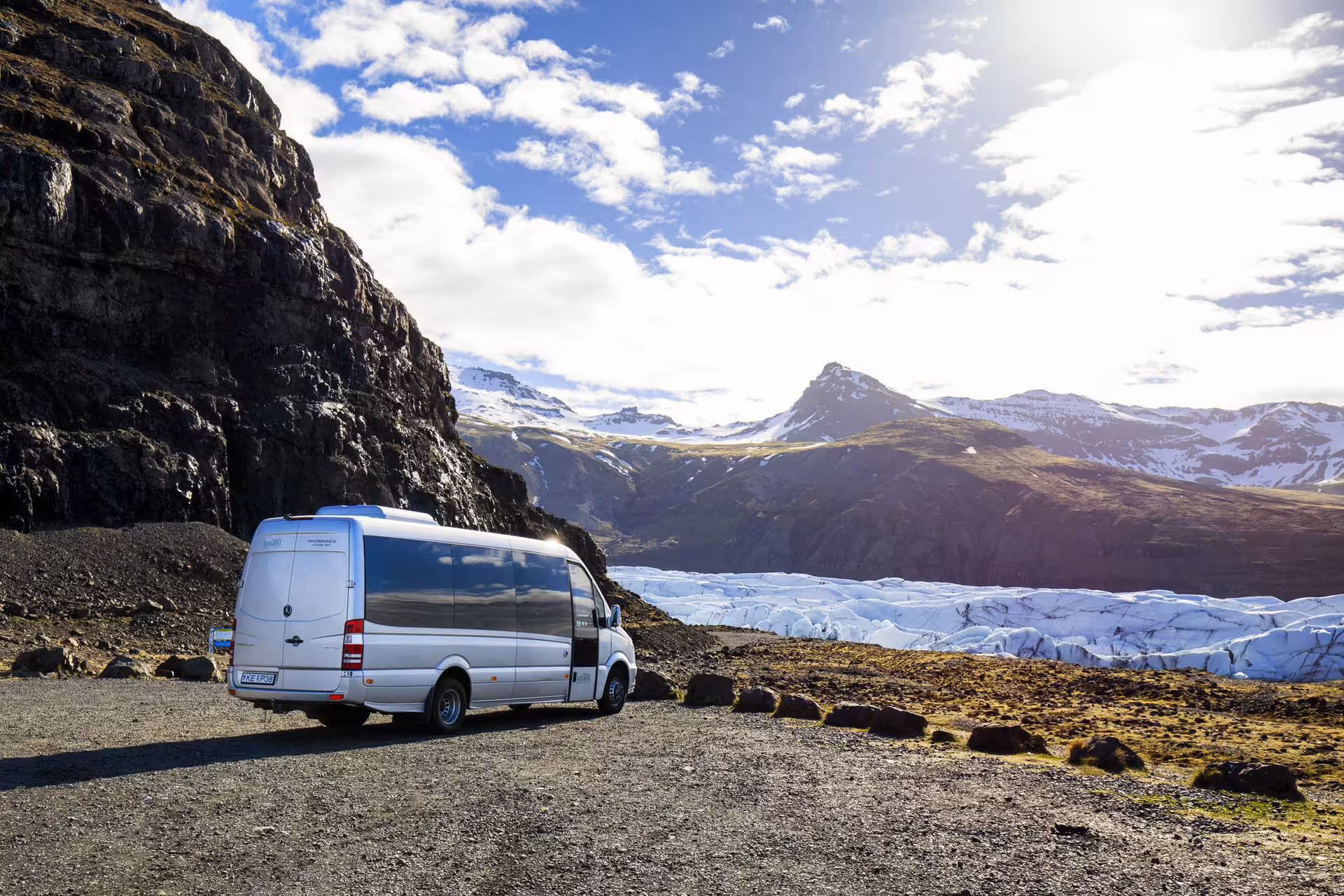 Silver camper van parked on gravel overlooking glacier and snow-capped mountains on Iceland's south coast