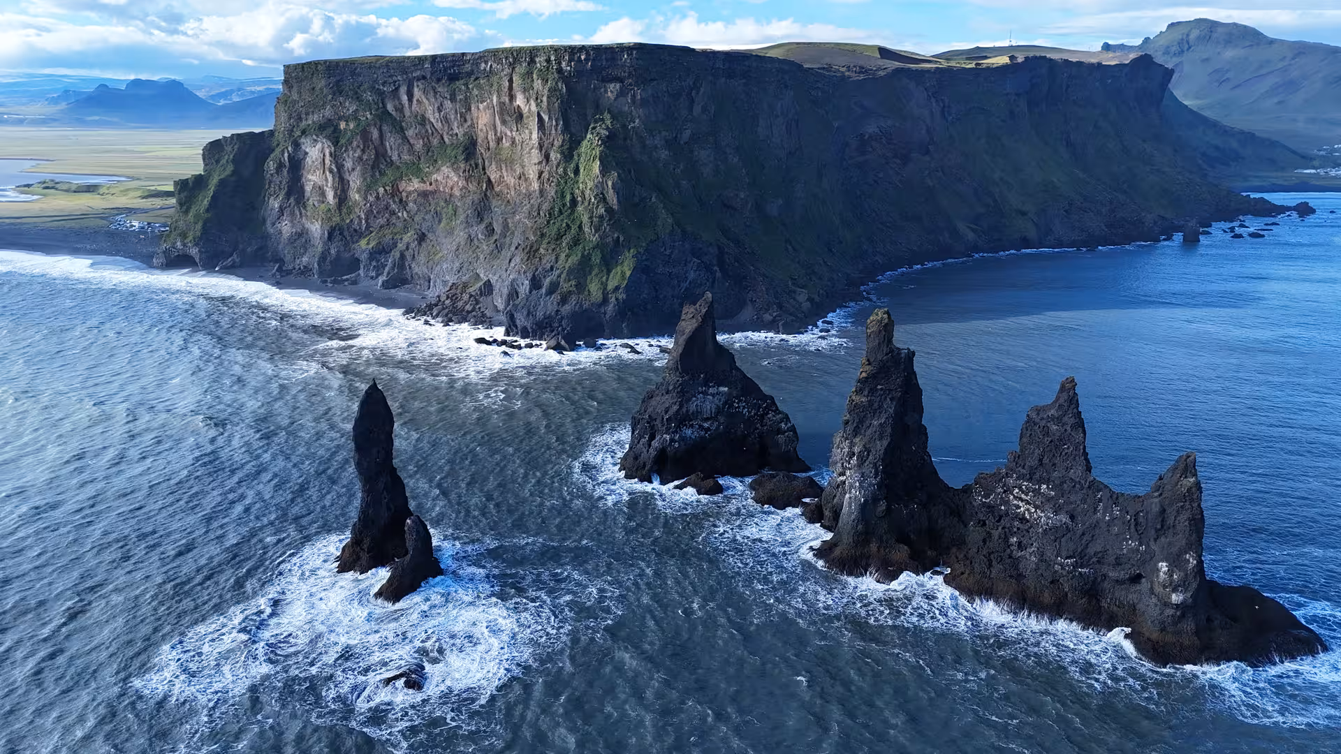 Aerial view of Reynisdrangar black basalt sea stacks rising from ocean waves near Iceland's south coast cliffs