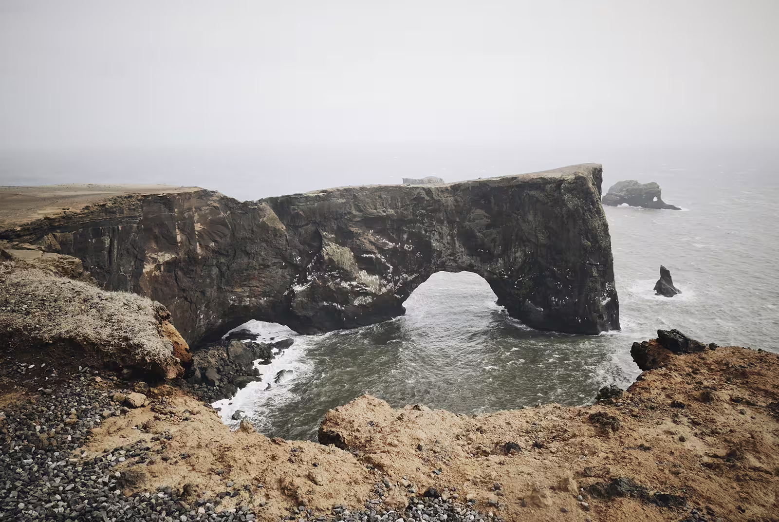 Natural rock arch on Iceland's south coast with crashing waves and misty sea views