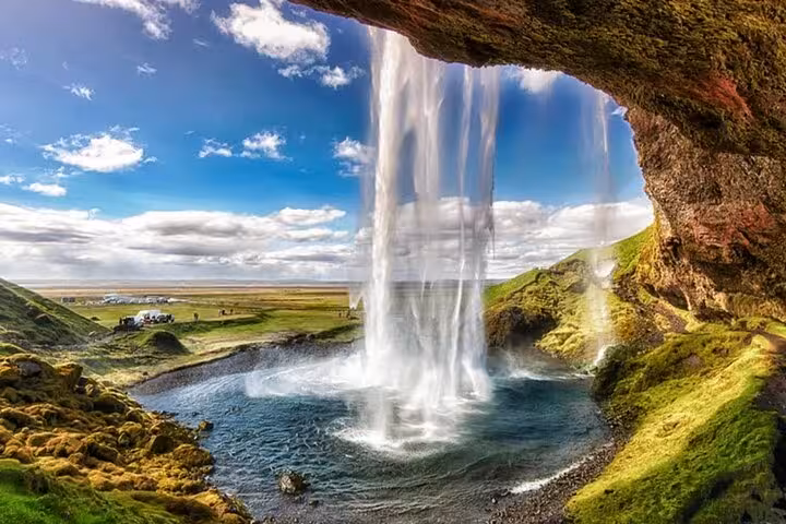 View from behind Seljalandsfoss waterfall on Iceland's South Coast with green landscape and blue sky